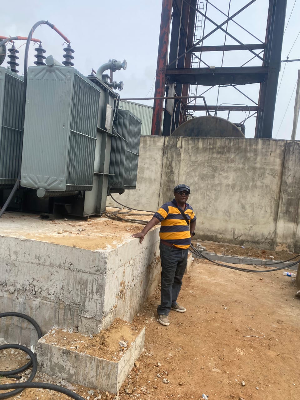 Engineer beside a large distribution transformer with bushings, cable terminations and a steel tower structure behind