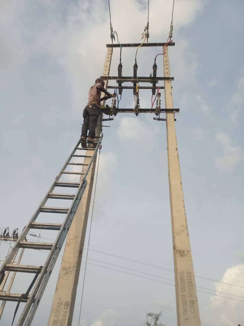 Linesman on a ladder working on pole-top switchgear, fuses and conductor terminations at height
