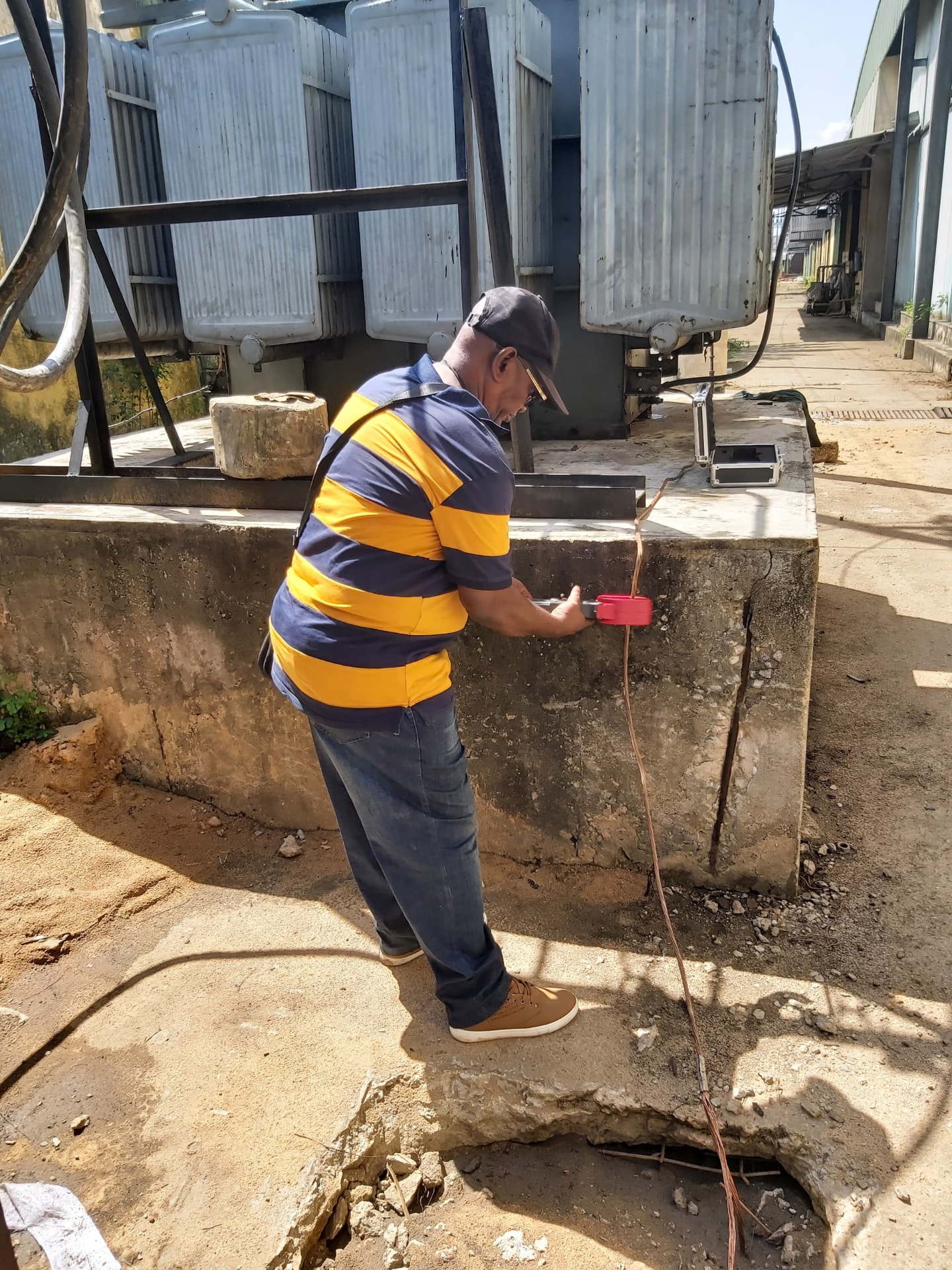 Engineer using a clamp-type test instrument on an earthing conductor beside a power transformer bank