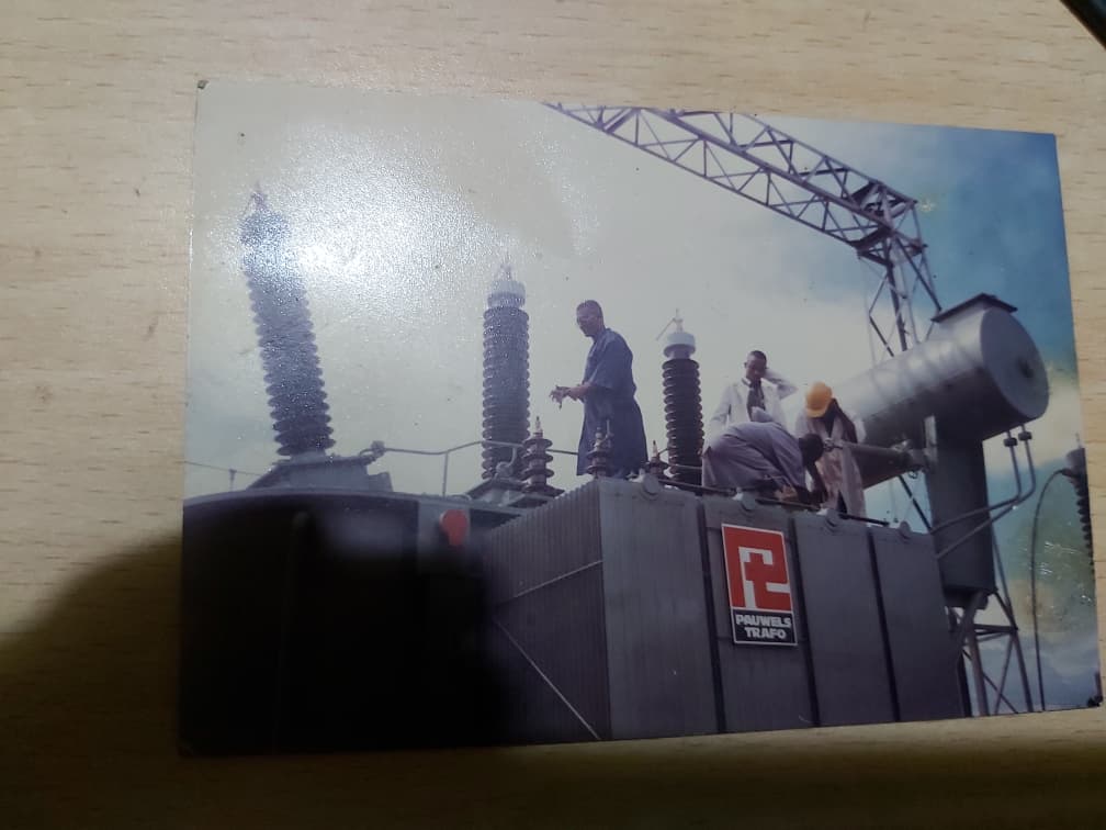Historic photograph of engineers working on top of a large power transformer with bushings and a crane above