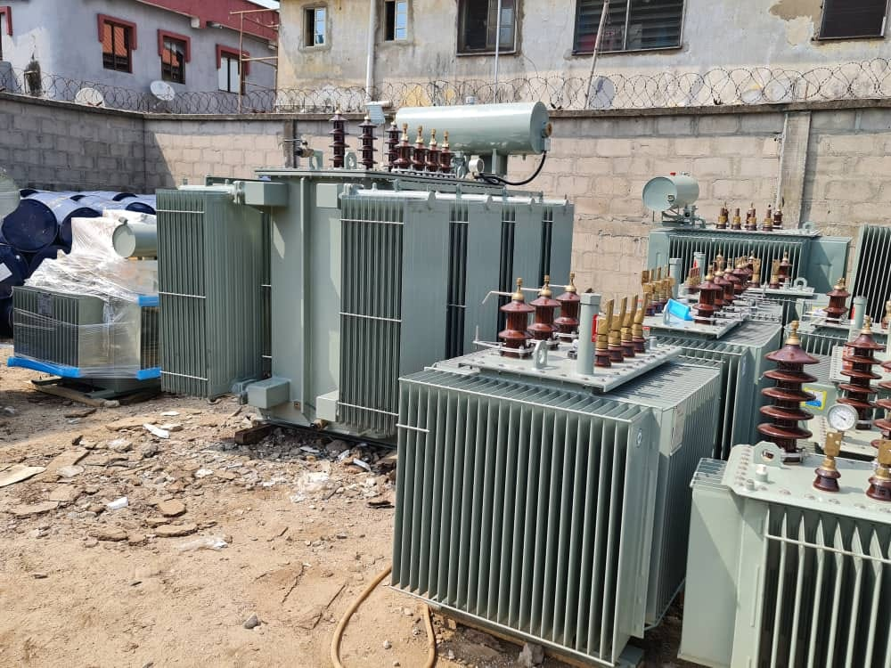 Group of distribution transformers in a site yard with lightning arresters, oil gauges and cable drums alongside