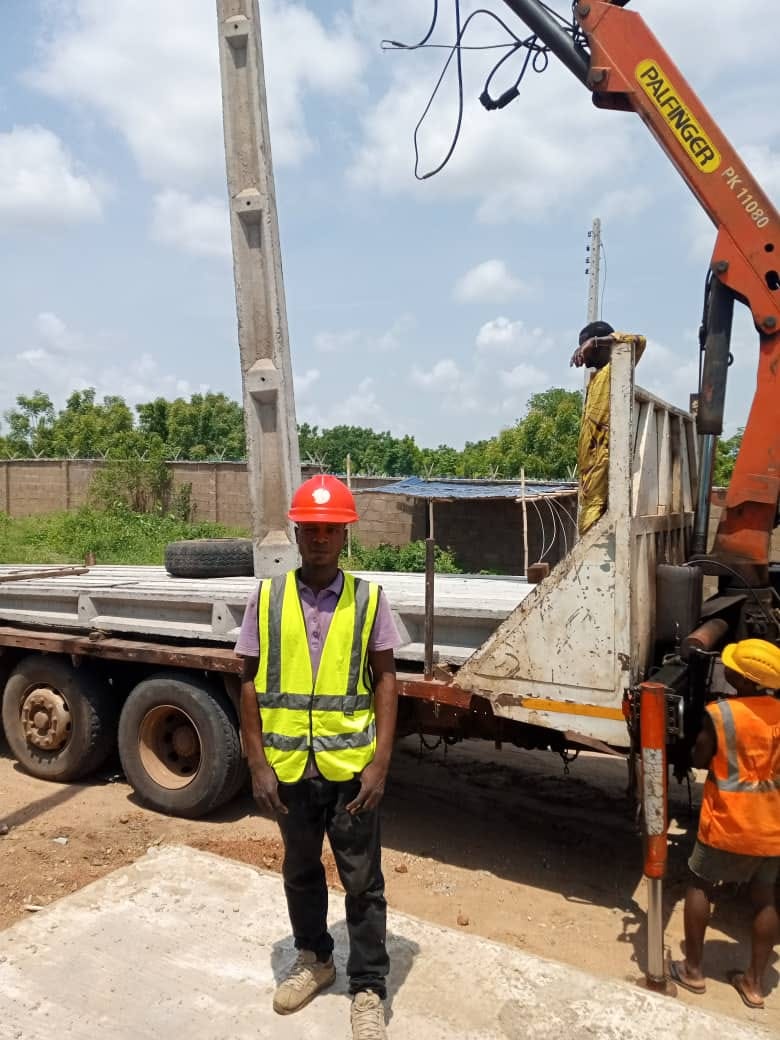 Site engineer in hard hat and high-visibility vest supervising delivery of concrete poles from a crane-mounted truck