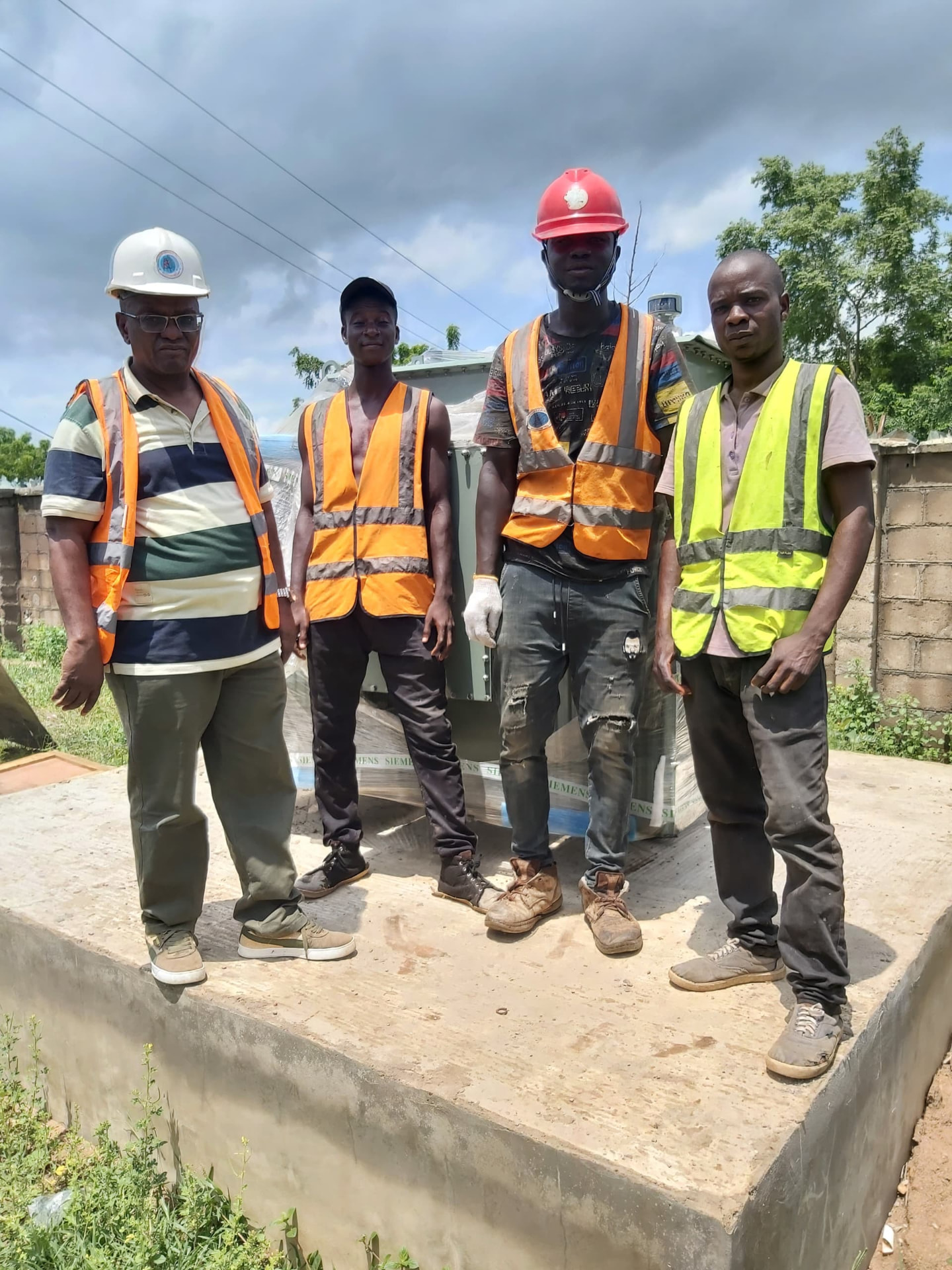 Four-man site team in high-visibility vests standing on a concrete plinth in front of a wrapped distribution transformer
