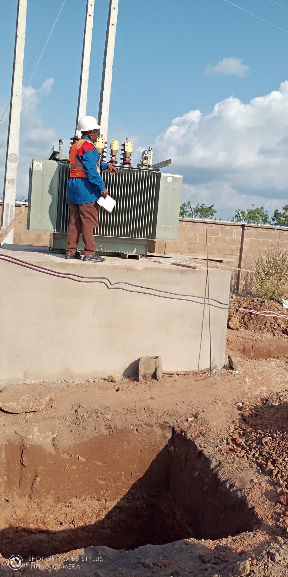 Engineer inspecting a newly positioned distribution transformer on a concrete plinth at a construction site