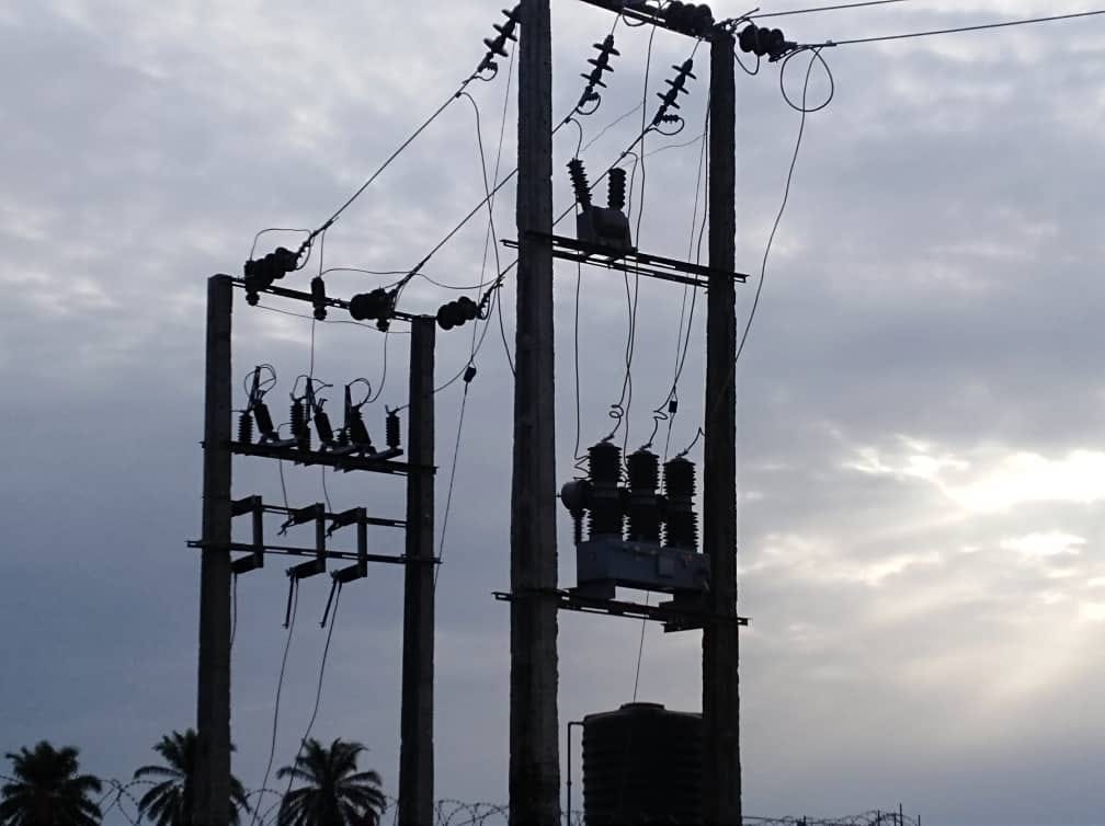 Silhouette of a pole-mounted distribution substation with transformer, isolators, insulators and drop-out fuses at dusk