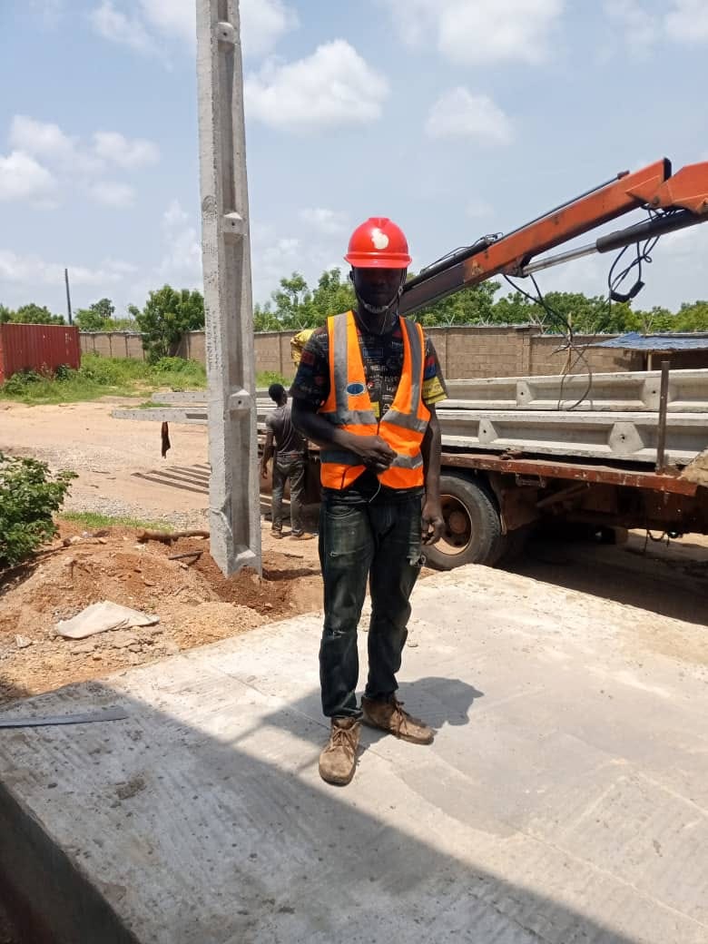 Site crew member in PPE beside a concrete pole being positioned by a crane truck during installation